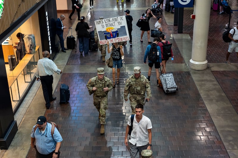 A protester holds a sign and follows members of the National Guard as they patrol Union Station in Washington DC. Photograph: Kent Nishimura/The New York Times
                      