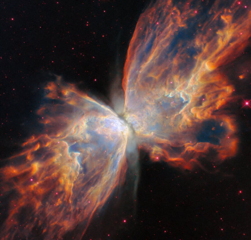 Colorful clouds of gas and dust form a butterfly-like shape in space, with bright orange, blue, and pink wisps radiating outward from a glowing center, set against a background of distant stars.