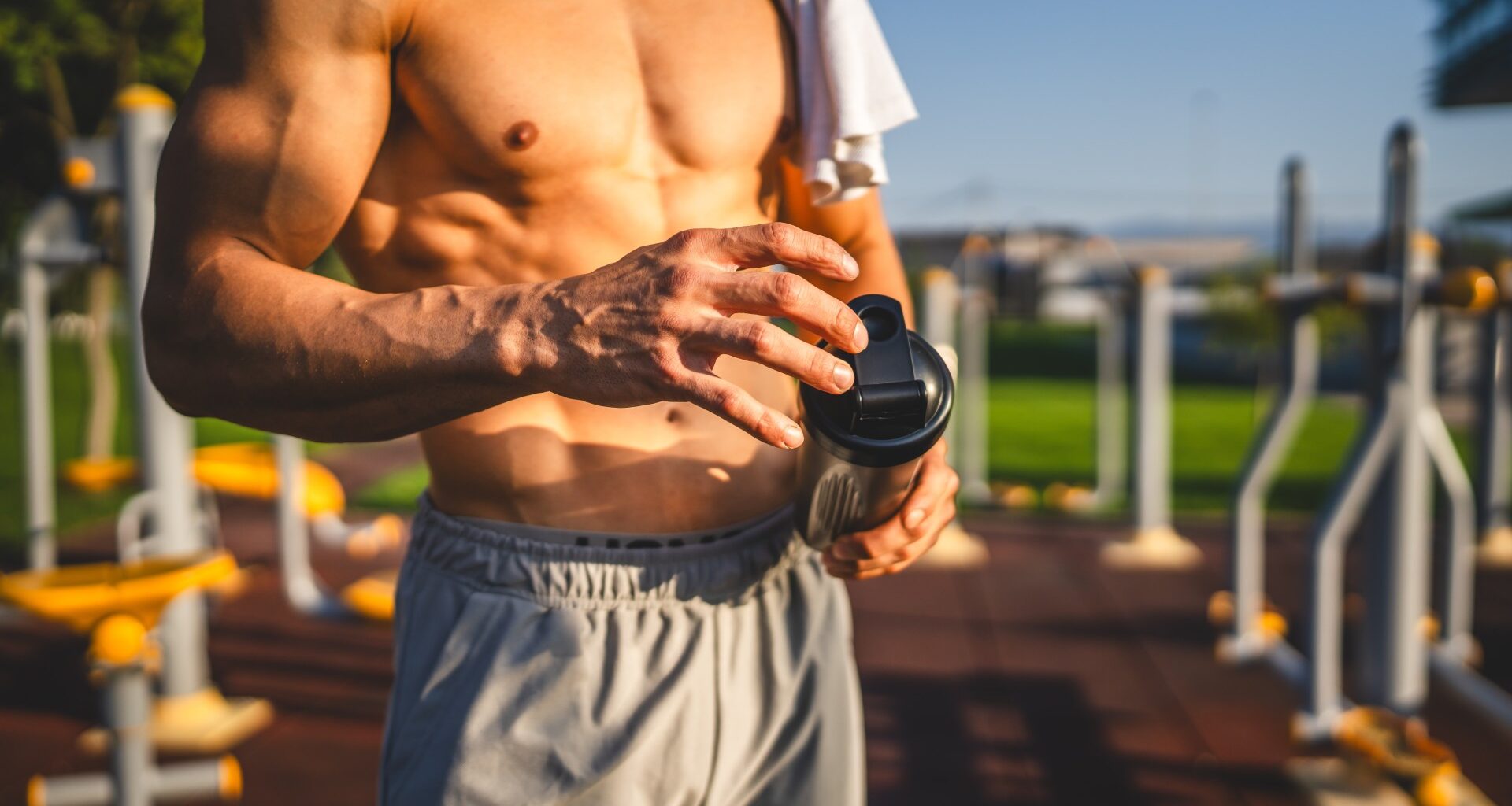 Muscled man holding a protein shaker outdoors
