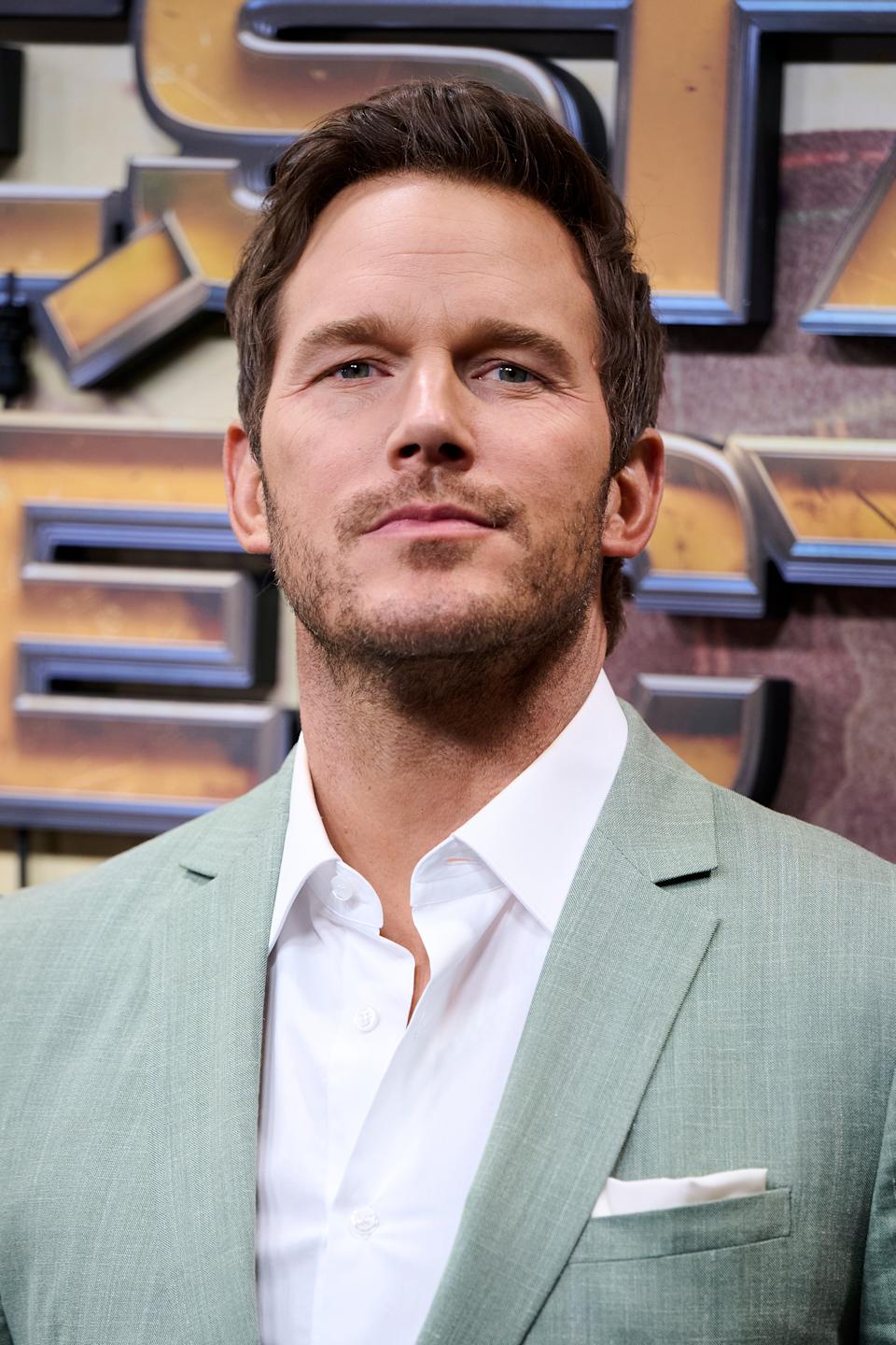 Chris Pratt in a suit on a media event backdrop, looking confidently forward