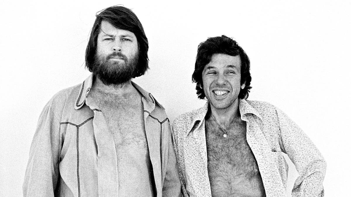 Brian Wilson with his shirt open posing next to Dr. Eugene Landy smiling also with his shirt open.