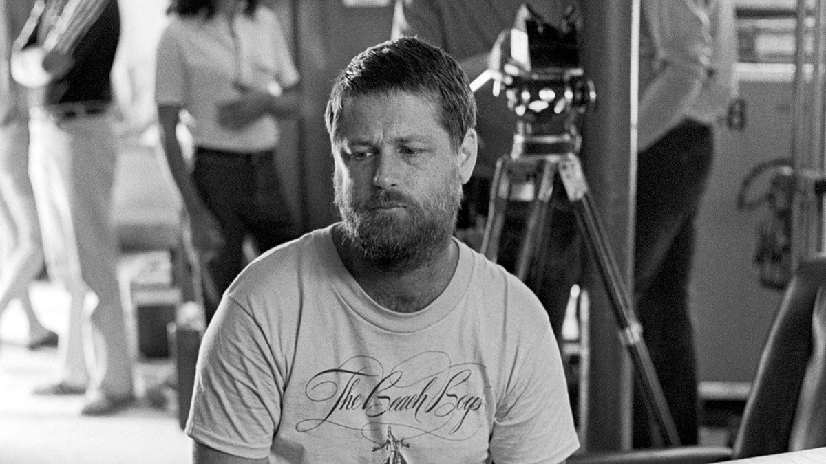 Brian Wilson looking somber wearing a t-shirt sitting on stage.