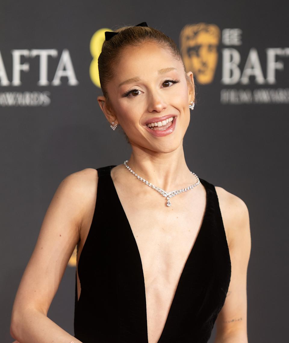 Ariana Grande in a sleeveless, deep V-neck gown poses on a BAFTA red carpet
