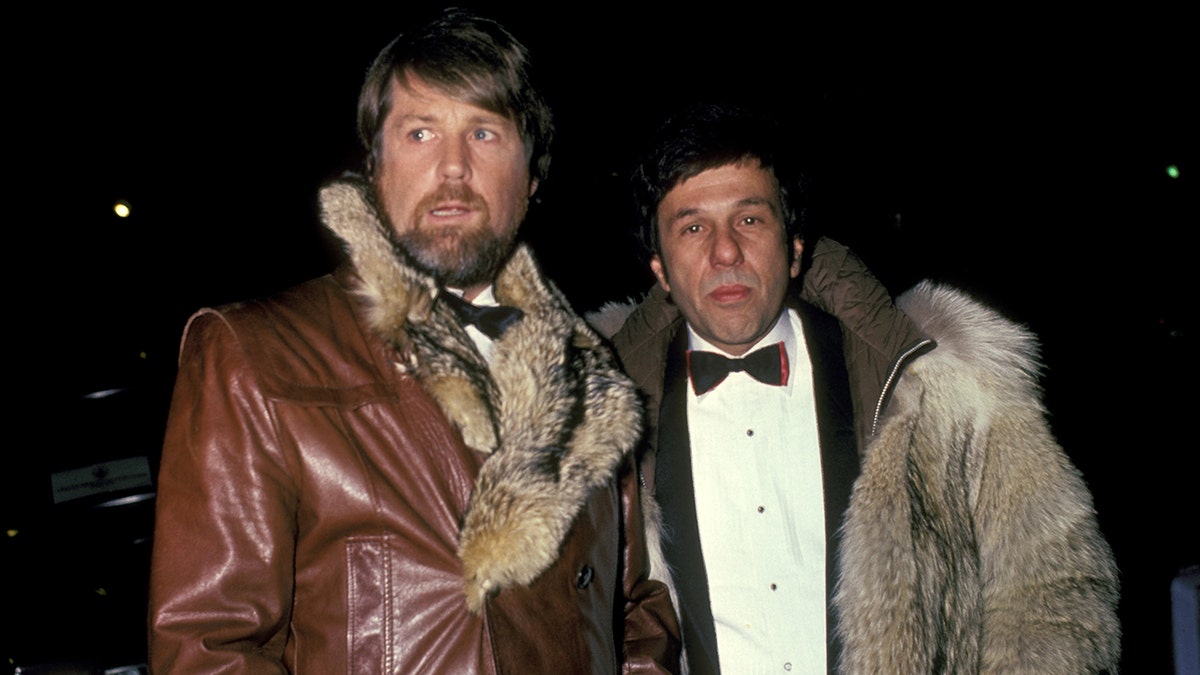 Brian Wilson wearing a leather fur coat standing next to Dr. Eugene Landy wearing an elegant tux.