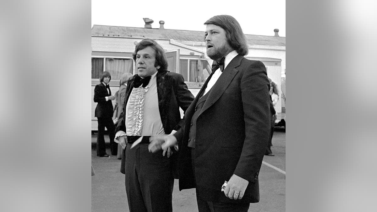 Brian Wilson in a tux standing next to Dr. Eugene Landy adjusting his pants.