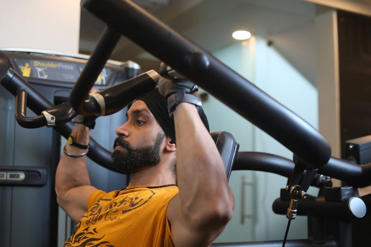 A bearded man in a yellow T-shirt using a weight machine in a gym