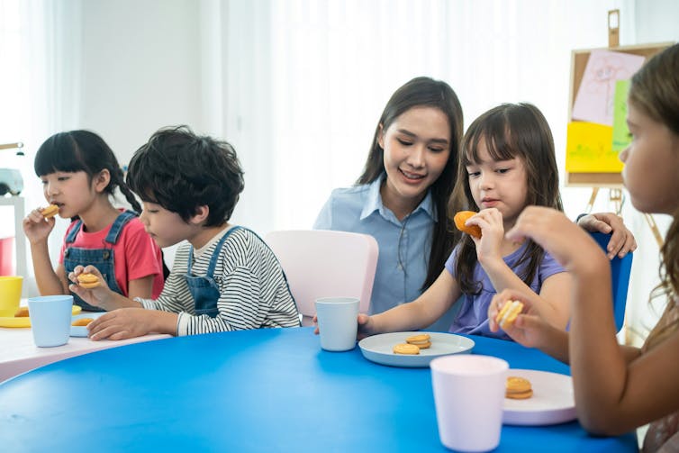 Children eating a snack at school with a teacher