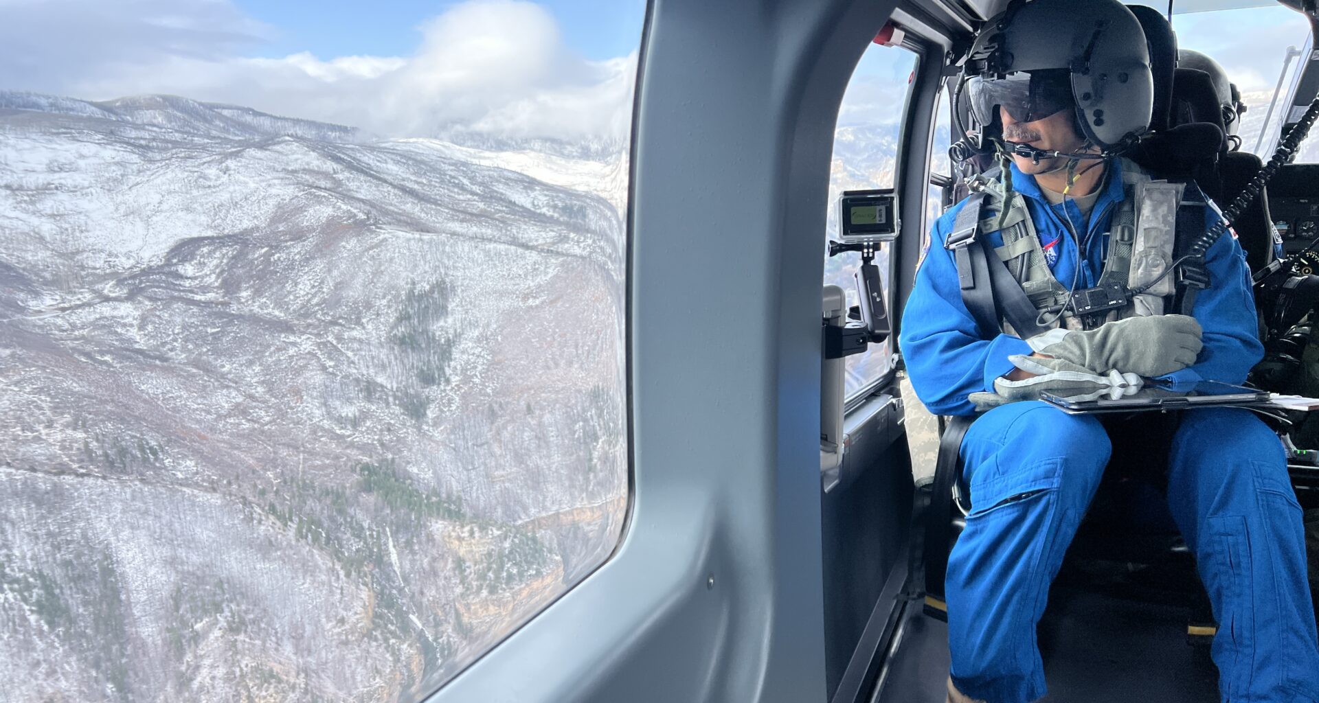 An astronaut in a helicopter looks out the window in their