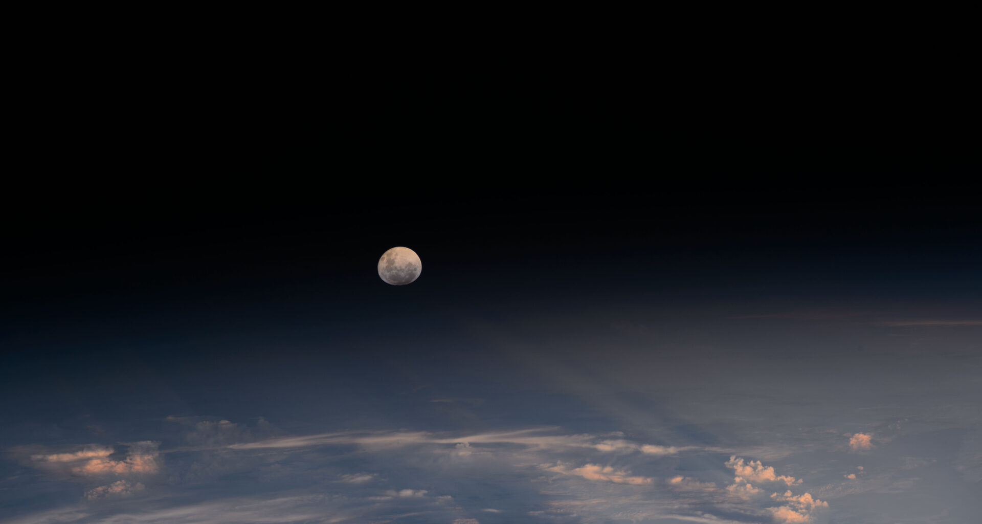 The Moon looks nearly full from the viewpoint of the International Space Station. Below, we can see the Moon's light being refracted by Earth's atmosphere. A few clouds can be seen at the bottom of the image.