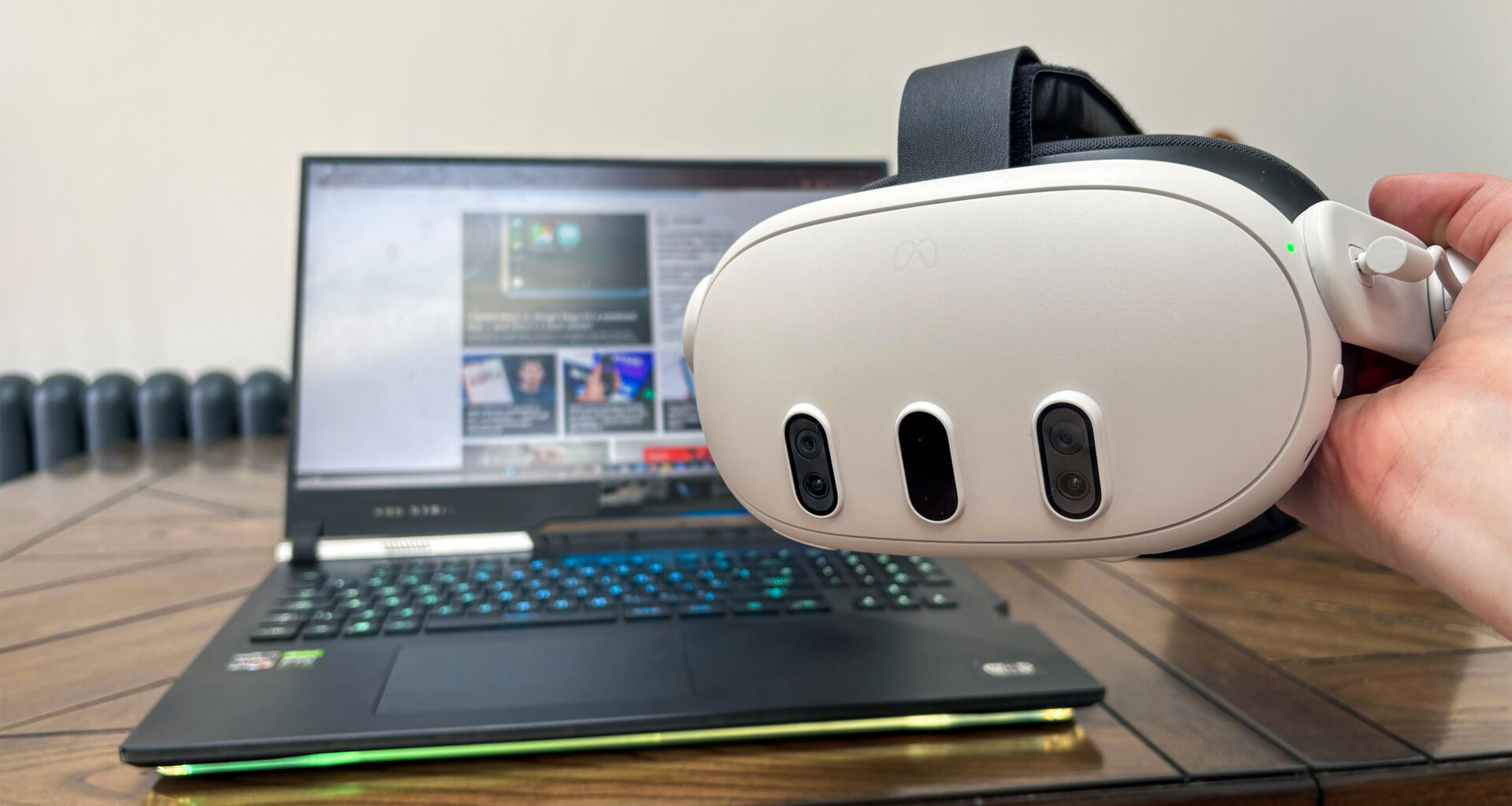 Meta Quest 3 held in hand with laptop on table in the background