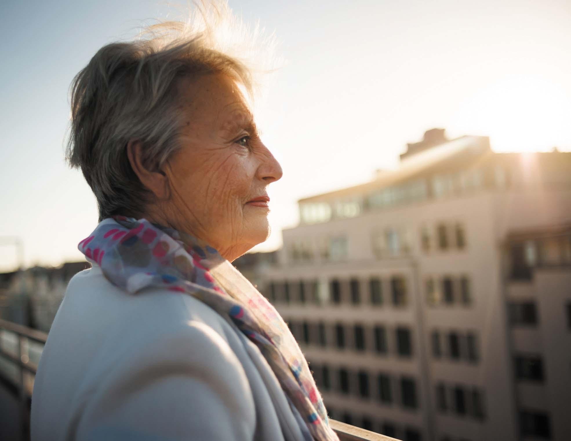 A mature woman on a rooftop looking out over a city.