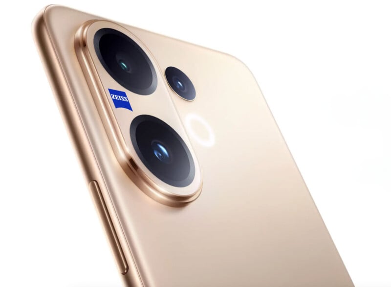 Close-up of a gold smartphone’s rear camera module featuring two large lenses, a smaller lens, a flash, and a Zeiss branding on one lens, against a plain white background.