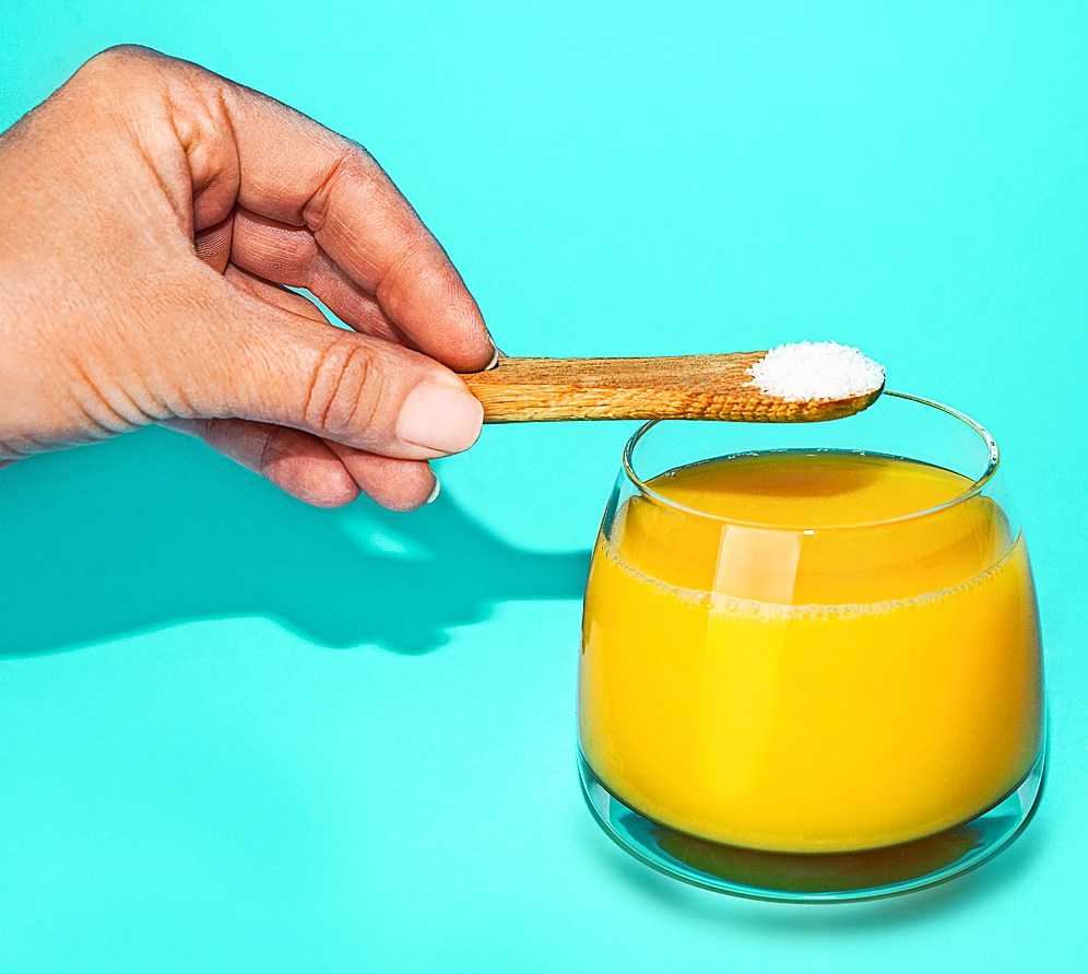 Hand adding protein powder to orange juice.