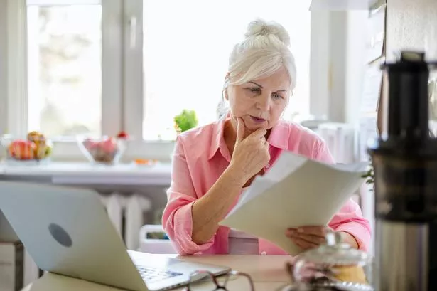 Senior woman working with laptop and documents at kitchen table at her home