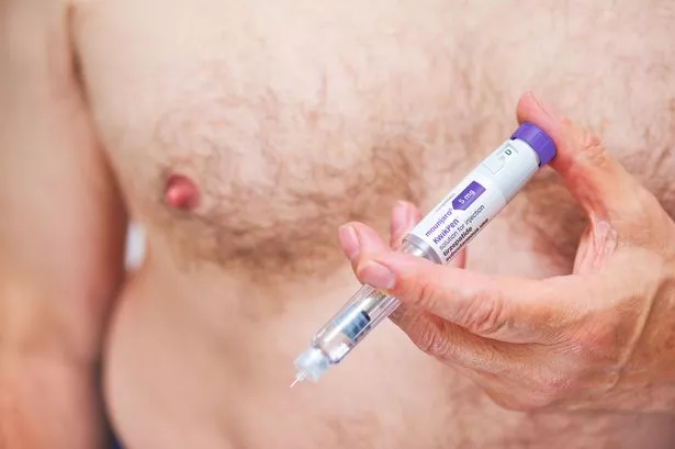 A man injects himself with a Mounjaro pen while standing topless