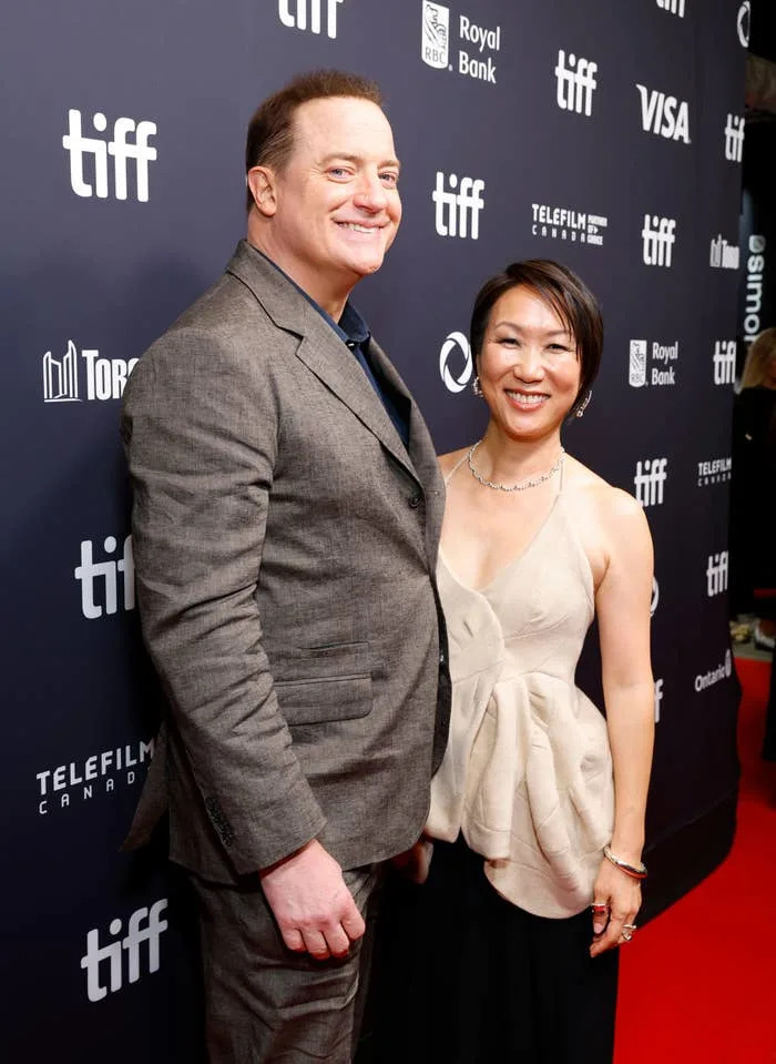 A smiling man in a tailored suit and a woman in an elegant gown pose together on the TIFF red carpet