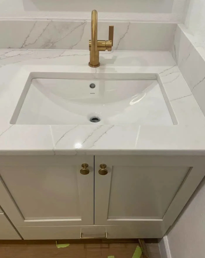 Bathroom vanity with a white marble countertop, modern rectangular sink, and a sleek gold faucet