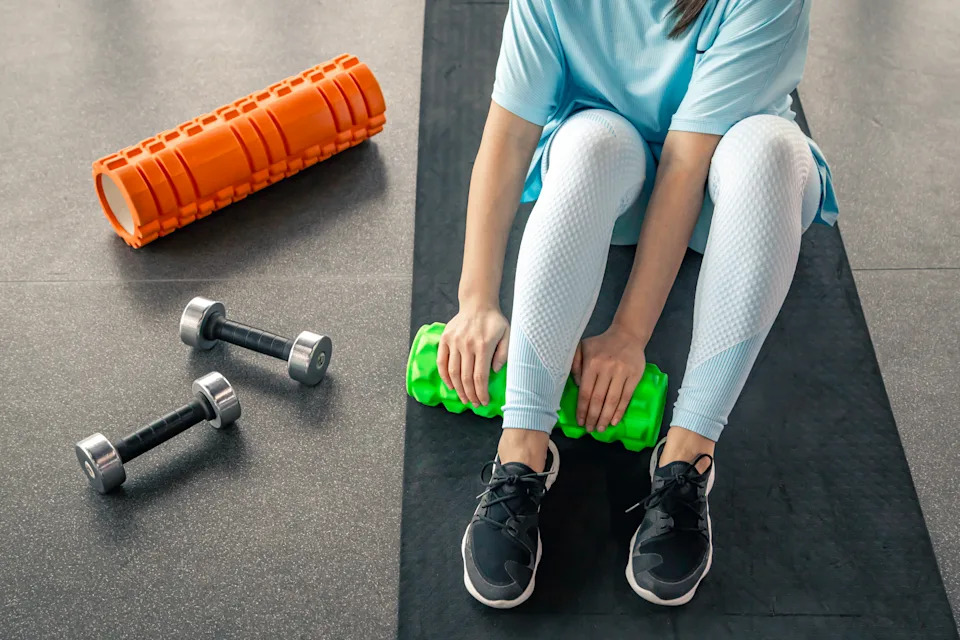 Woman works the fascia of the calf muscles with a massage foam roller on the floor in a gym.