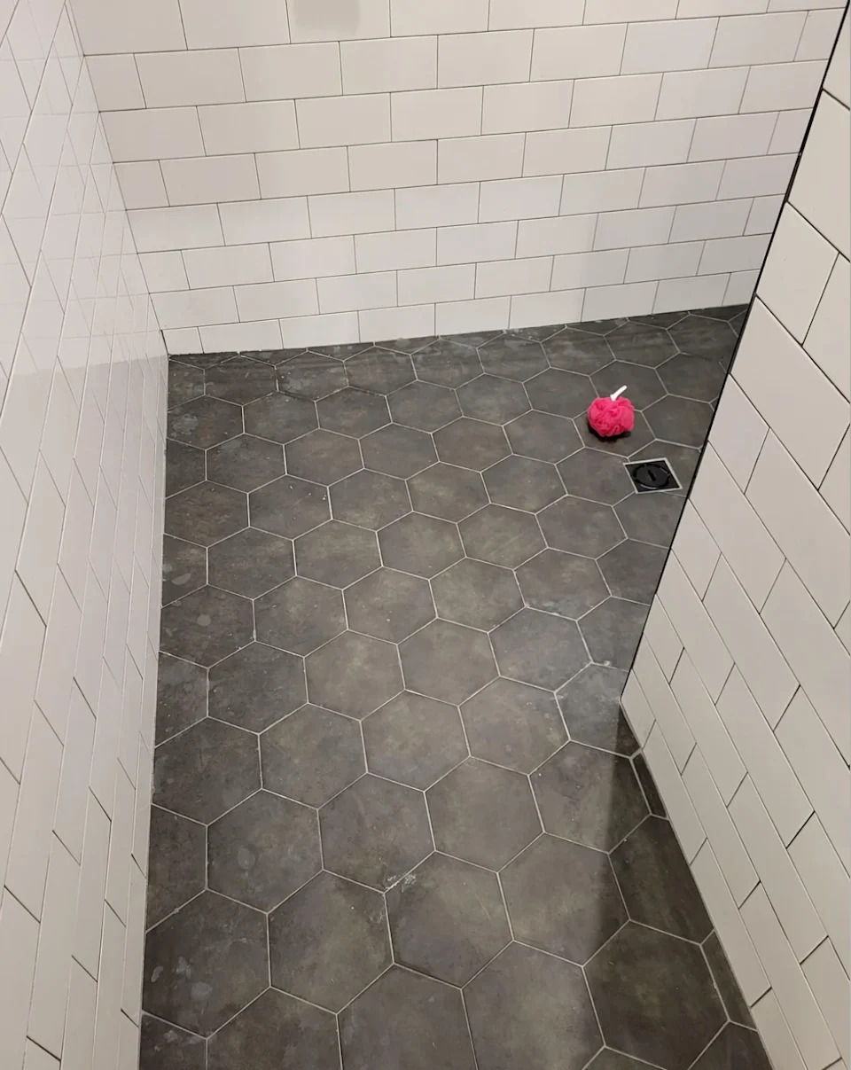 Bathroom with hexagonal floor tiles and white tiled walls. A pink object is on the floor near a drain