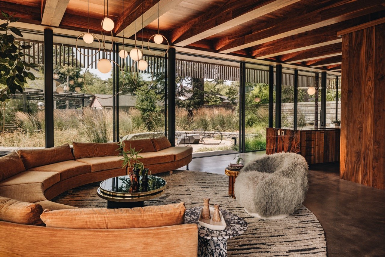 The living area in this Portland house features the reupholstered Milo Baughman sofa, Studio SORS lounge chair covered in New Zealand sheepskin, and Pablo chandelier above the concrete floors with metal veining