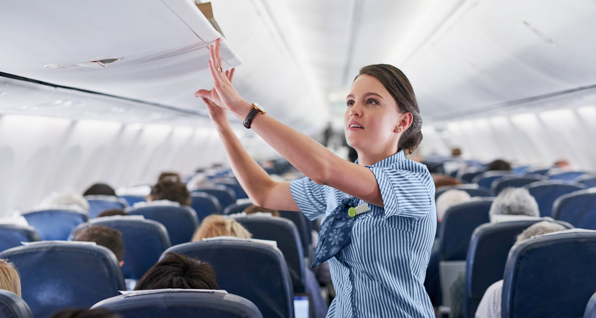 Shot of a young air hostess closing the overhead compartment on an airplane.
