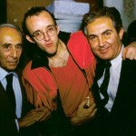 Two gentlemen in suits with a young bespectacled man in red.