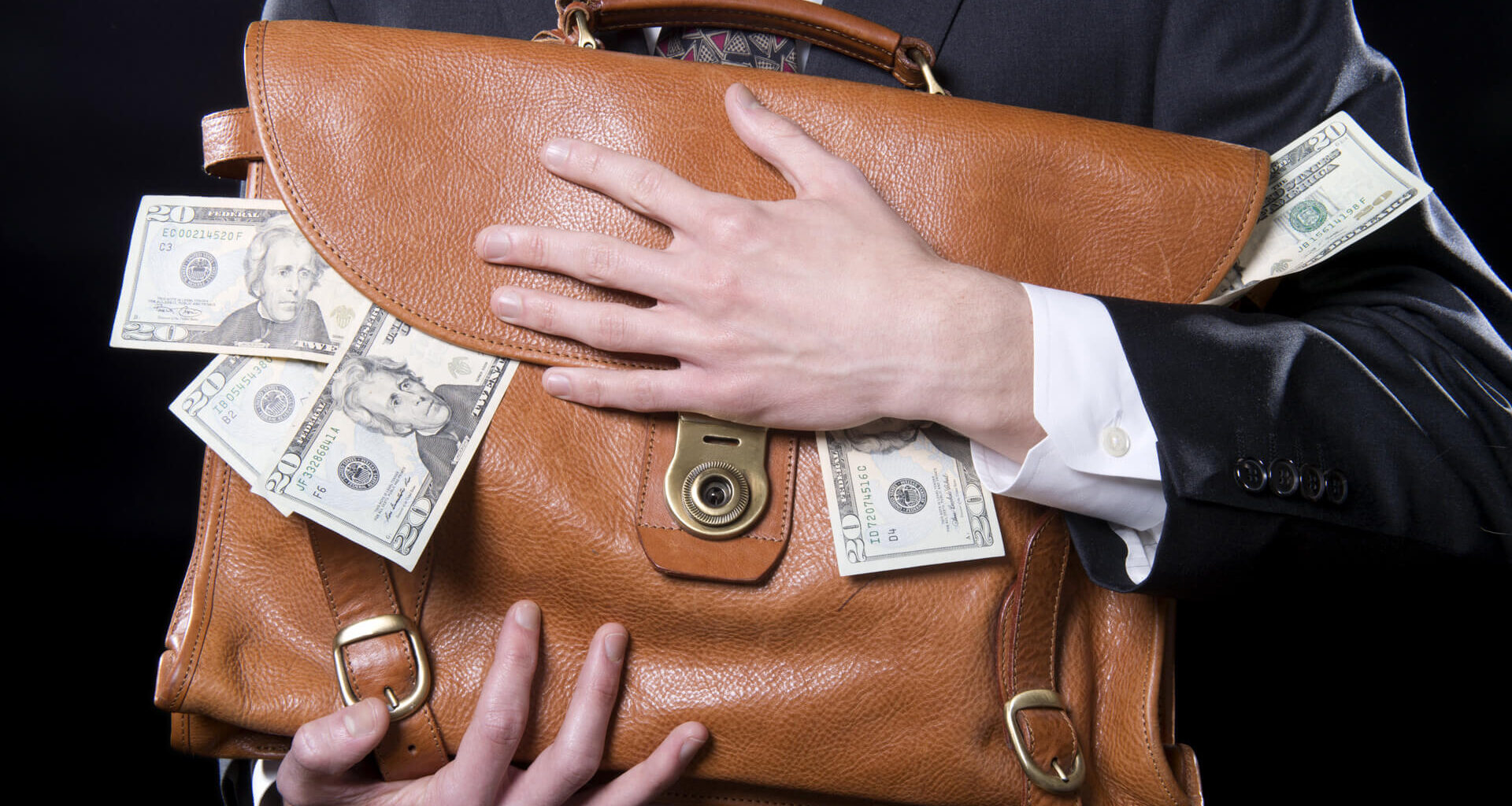 Closeup of man holding briefcase with money spilling out close to his chest.