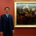 A man in a suit standing beside a painting.