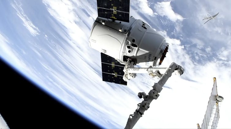 A conical, white spacecraft with 2 rectangular solar panels in space, with the Earth in the background.