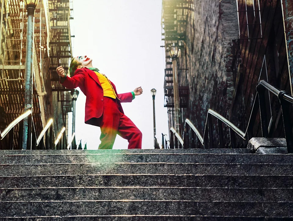 Person in bright suit dances on city steps, reminiscent of a movie scene. Urban setting with dramatic pose captures a sense of freedom and joy