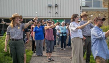 A group of people stand outside holding white Styrofoam balls on a stick with arms outstretched to model moon phases.