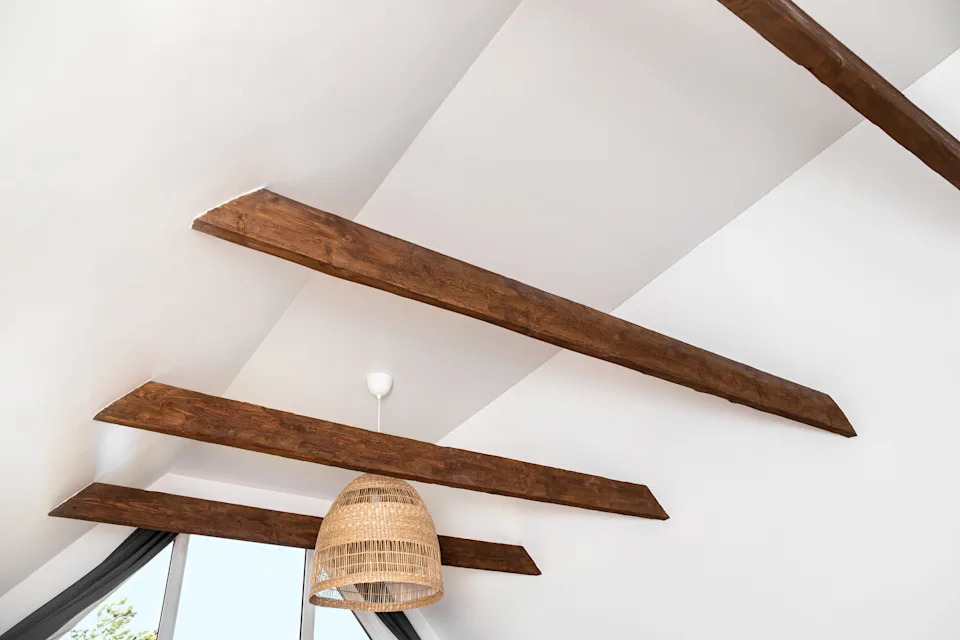 Ceiling view with wooden beams and a rattan pendant light hanging, near large window with curtains