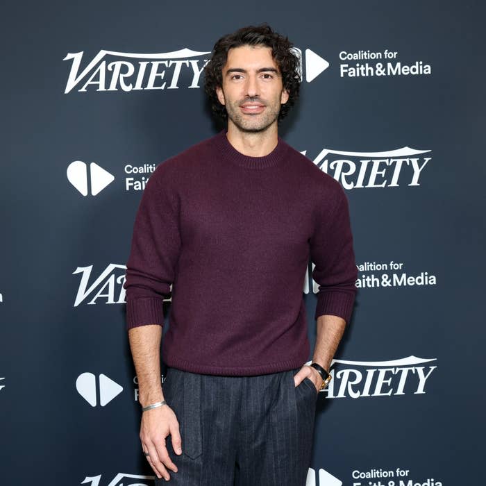 Person in a sweater and trousers on a red carpet, posing at a Variety event backdrop