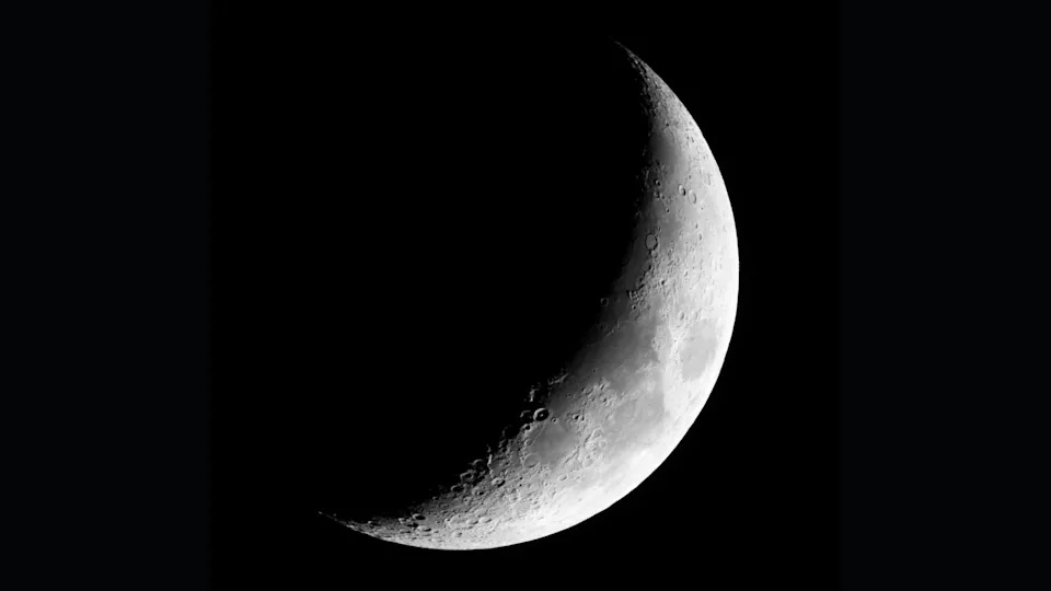 A waxing crescent moon is pictured with its right side lit by sunlight and its left hidden in shadow against a black sky.