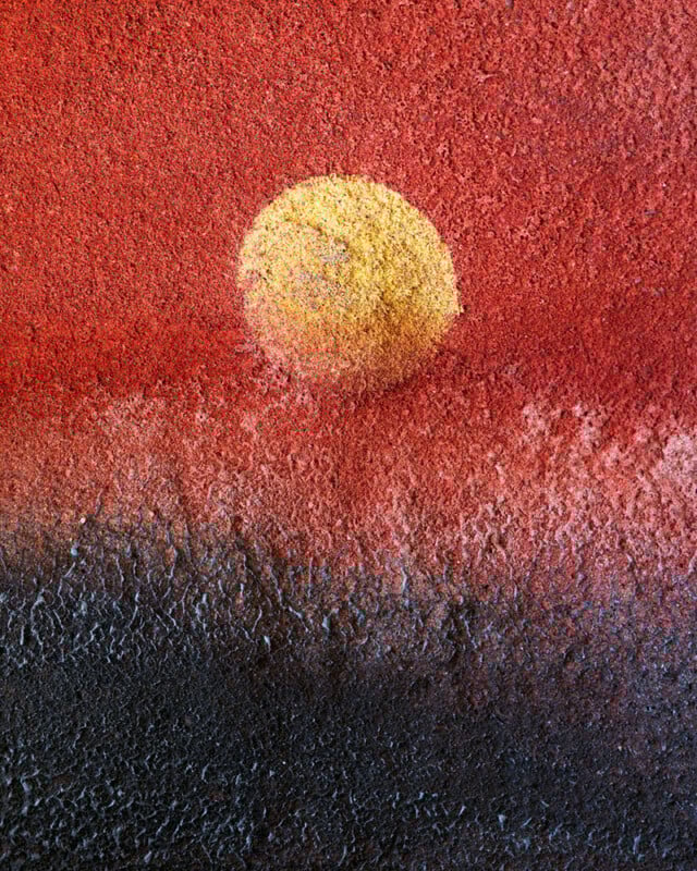 A textured surface painted to resemble a landscape, with a yellow circle like a sun or moon set against a red sky and dark, rough terrain at the bottom, creating an abstract sunset or sunrise effect.