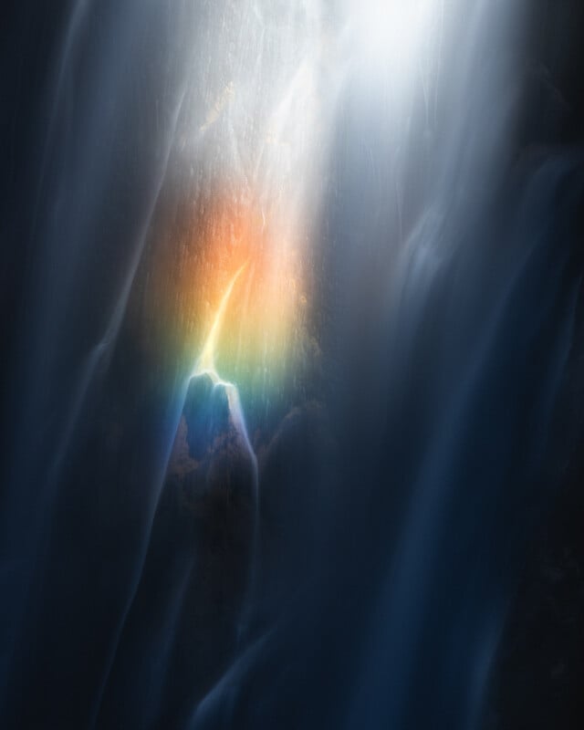 A misty waterfall with soft, flowing water illuminated by a small, vivid rainbow in the center, surrounded by a dreamy, ethereal glow.