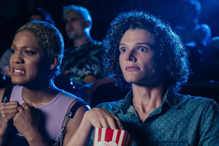 Two people in a theater look surprised and anxious, holding popcorn