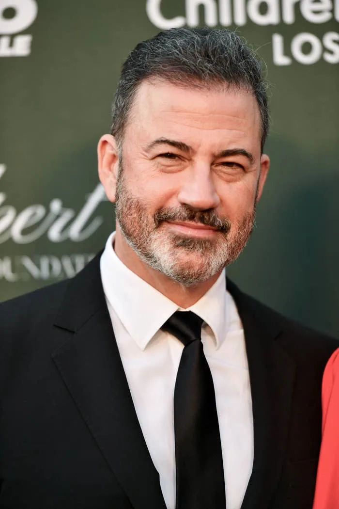 Person in a suit and tie at an event backdrop, smiling