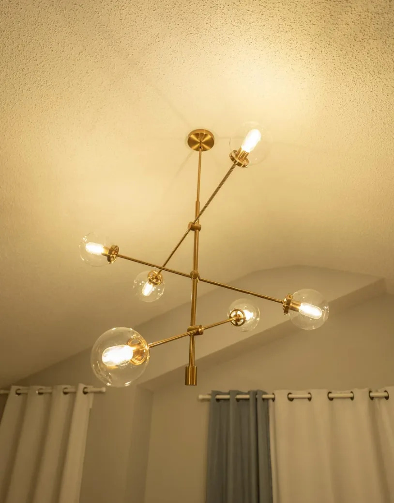 Modern chandelier with six exposed bulbs in a minimalist room with curtains and textured ceiling