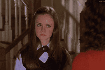 Young woman in school uniform frowns and looks to the side, appearing upset or displeased, standing in a hallway setting