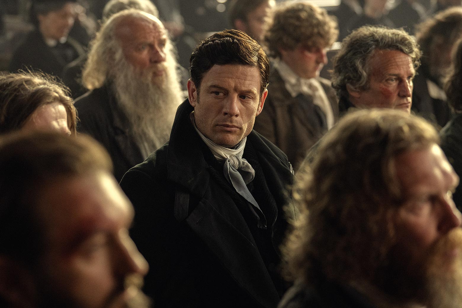 A man looks around angrily in a crowd in a scene from the show.