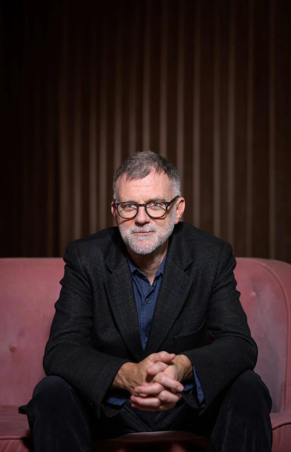 A director in glasses leans in, sitting on a sofa.