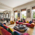 a room with large windows, sofas, and many paintings on the wall.
