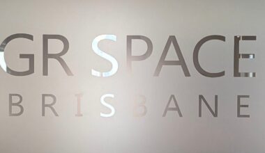 Frosted glass with cut-out letters partially reading "GR SPACE BRISBANE," with the background faintly visible through the transparent text.