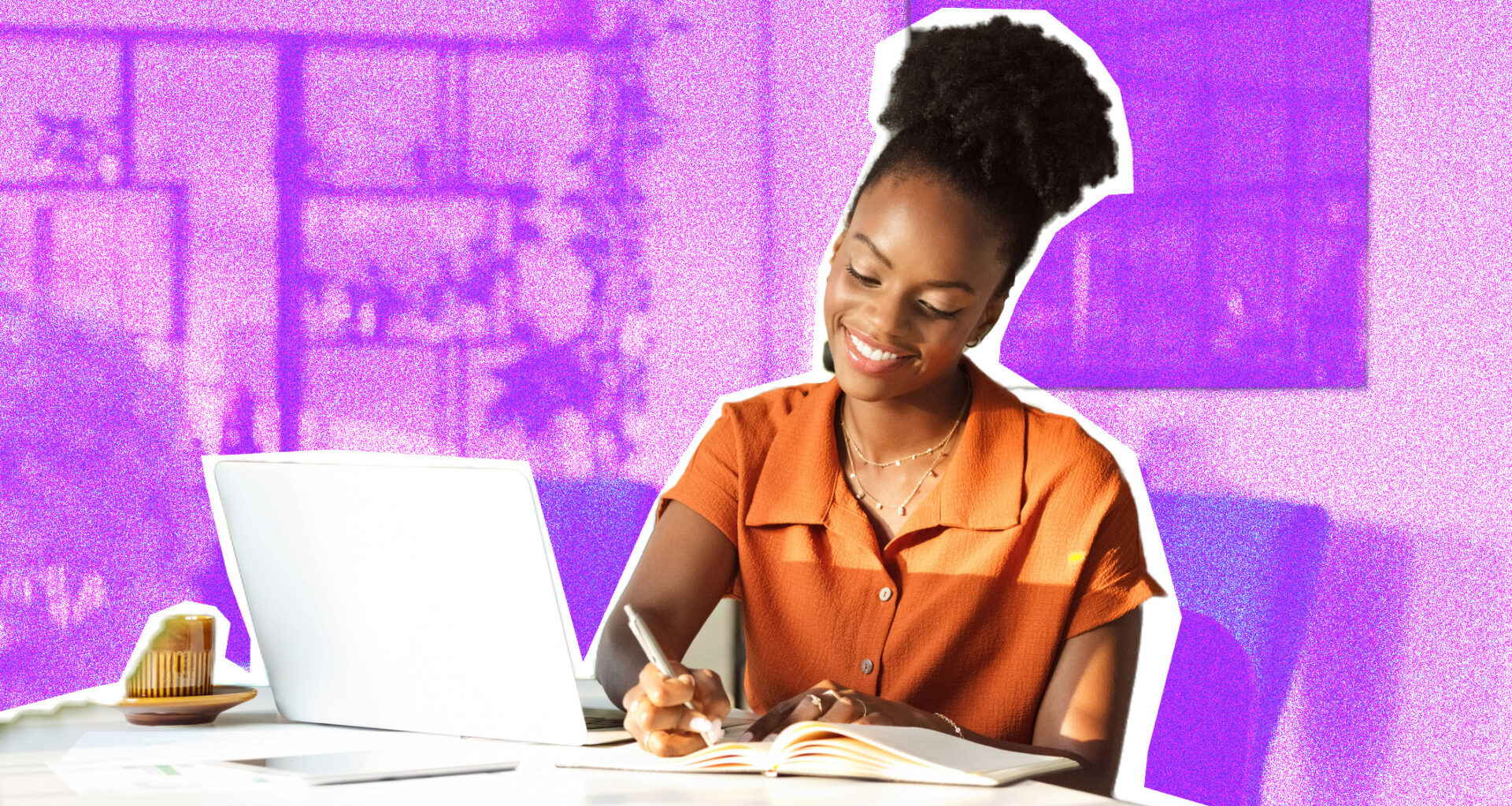 A woman sitting at a desk, writing in a notepad. A laptop is also on the table.