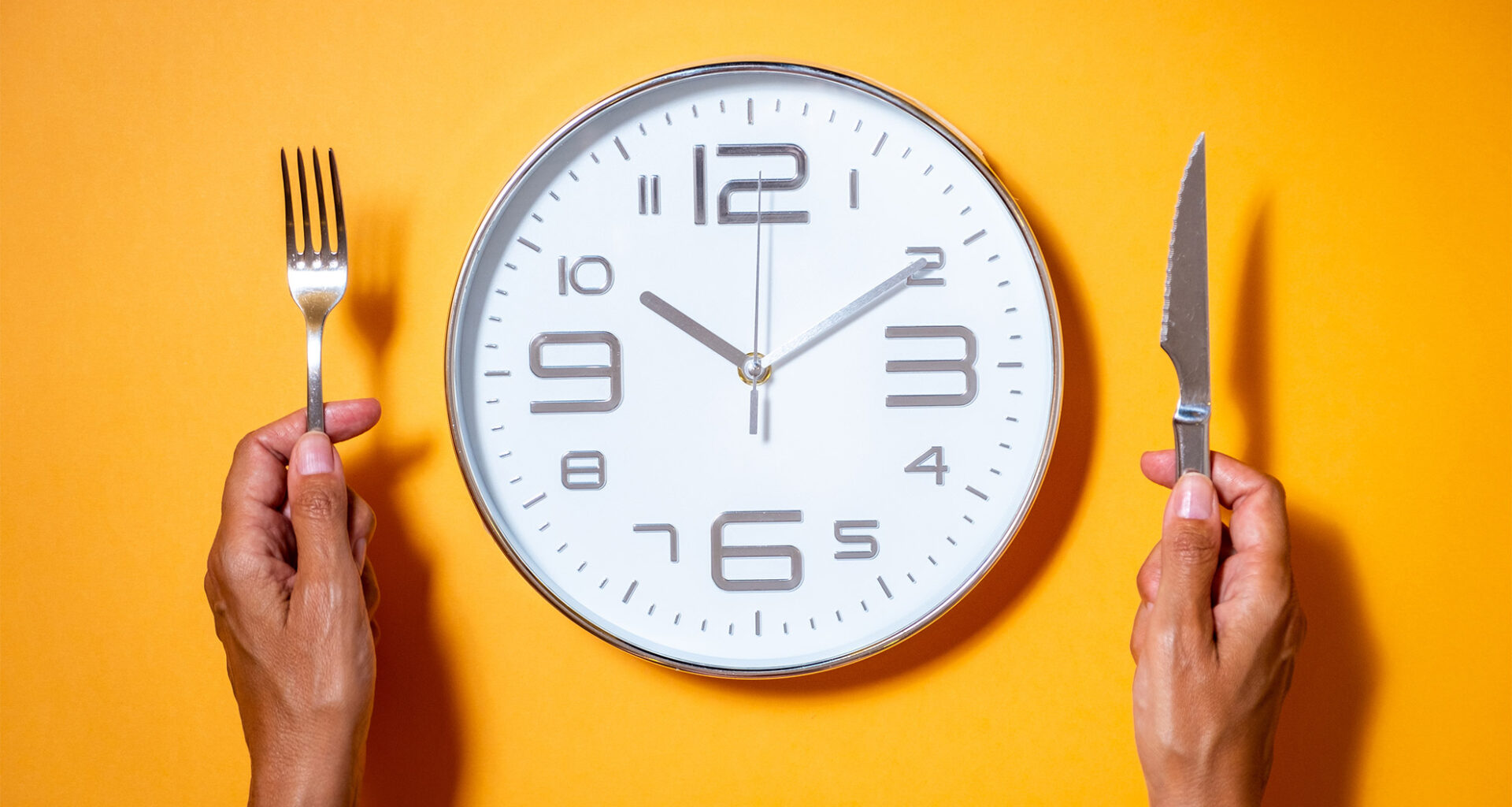 A clock as if it were a plate of food next to a hands holding fork and knife.