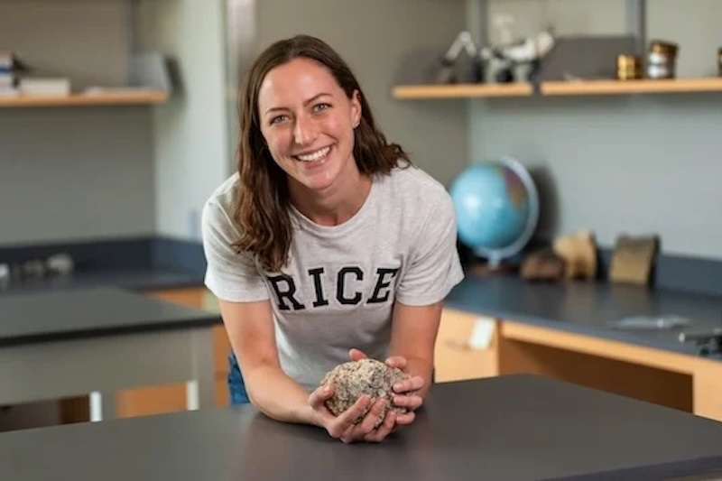 Smiling woman standing in a lab room, wearing a white t-shirt that says 'Rice.'