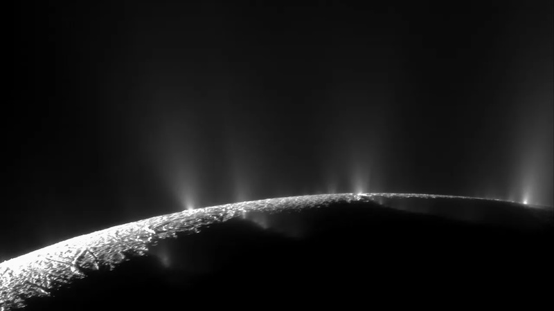 Organics in Enceladus' plumes: Sunlit limb of planet-like body, with jets of vapor erupting upward against a black background.