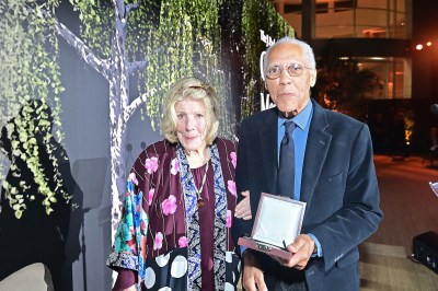 A woman in a dress beside a man in a suit holding an award.