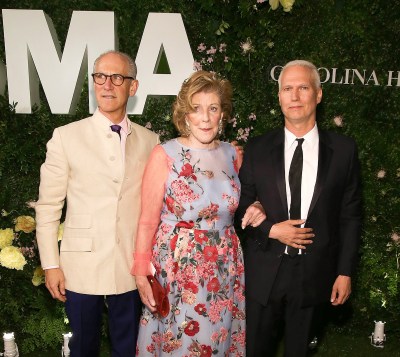 Two men in suits and a woman in a dress on a red carpet.